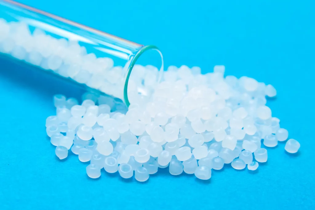 Polymer resin pellets scattered from a glass container on blue surface